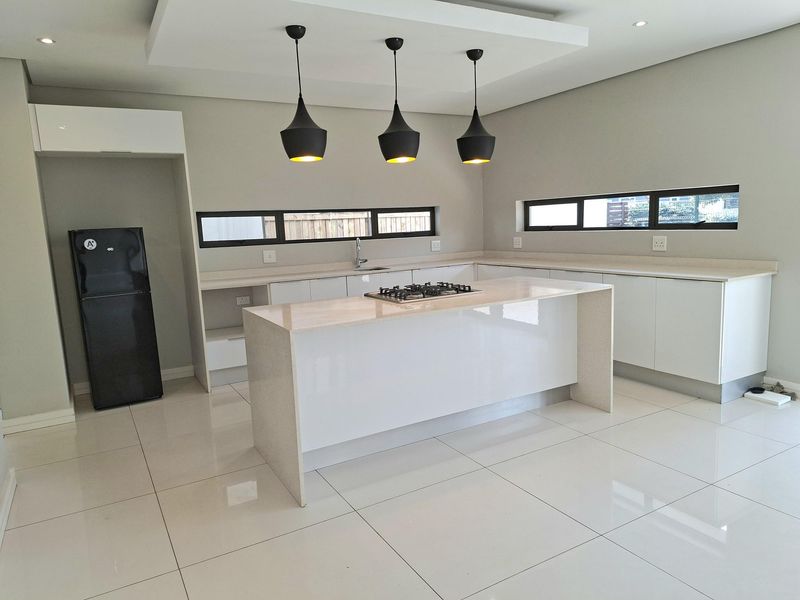 Modern kitchen featuring a central island with a gas hob, sleek white cabinetry, stone countertops, and polished tiled flooring.