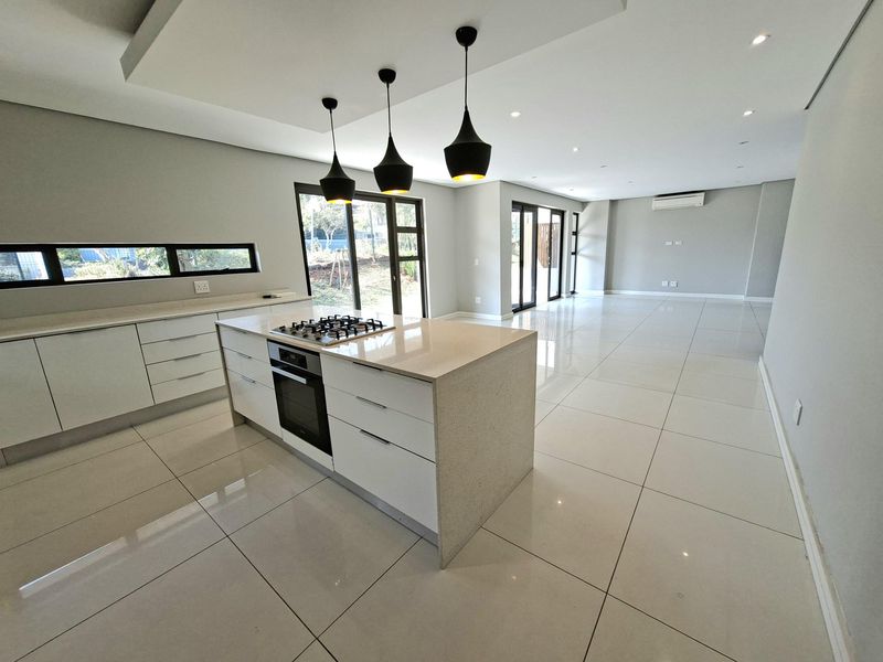 Spacious open-plan kitchen and living area featuring a central island with gas hob, modern cabinetry, stone countertops, and large sliding doors to the exterior.