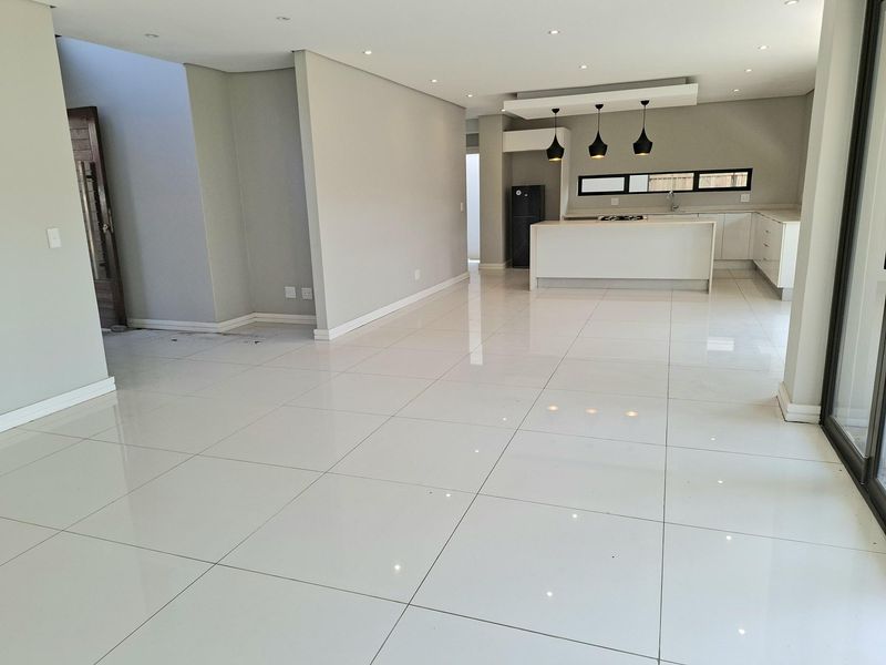 Spacious open-plan living and kitchen area featuring modern white cabinetry, a central island, sleek porcelain floor tiles, and recessed lighting throughout.