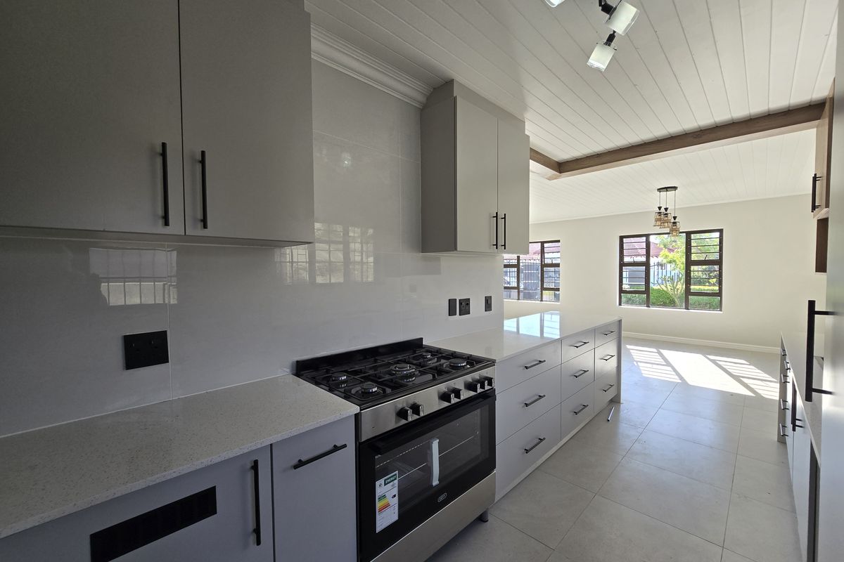 Modern kitchen featuring sleek grey cabinetry, quartz countertops, a gas hob, and an integrated oven, flowing into an open-plan living area.