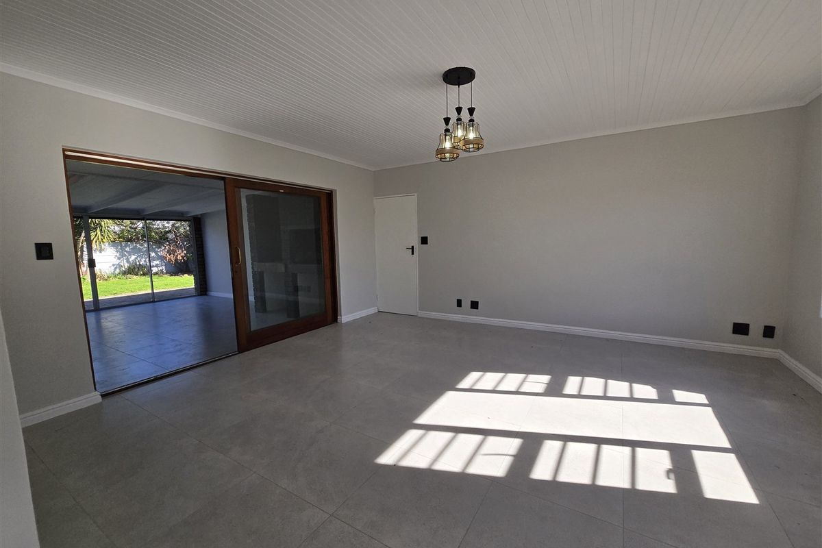 Spacious, light-filled living room featuring large sliding glass doors that open to an outdoor patio area, finished with modern floor tiles.