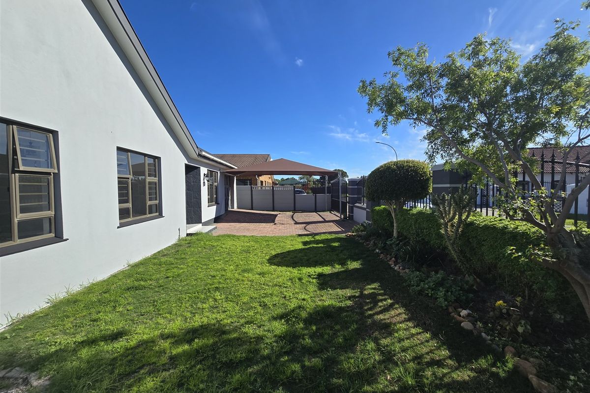 A well-maintained rear garden featuring a paved driveway, a covered carport, and established landscaping with a neat lawn.