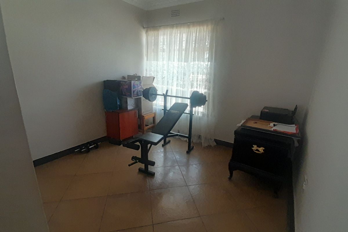A standard bedroom featuring tiled flooring and a window with natural light, currently utilized as a home gym space.
