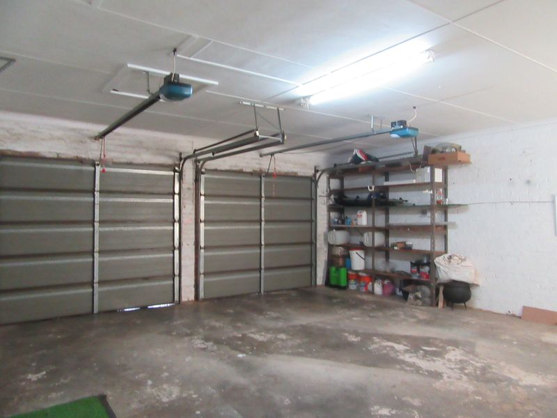 A functional double garage featuring automatic door openers, painted brick walls, and concrete flooring, providing ample space for vehicle storage and utility use.