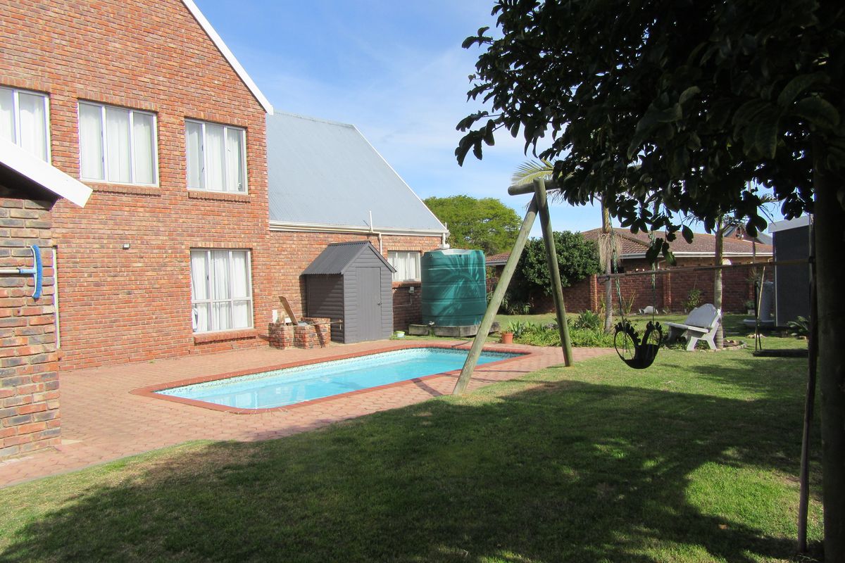 Rear exterior view featuring a swimming pool, brick paved patio area, water tank, and a spacious garden with established lawn.