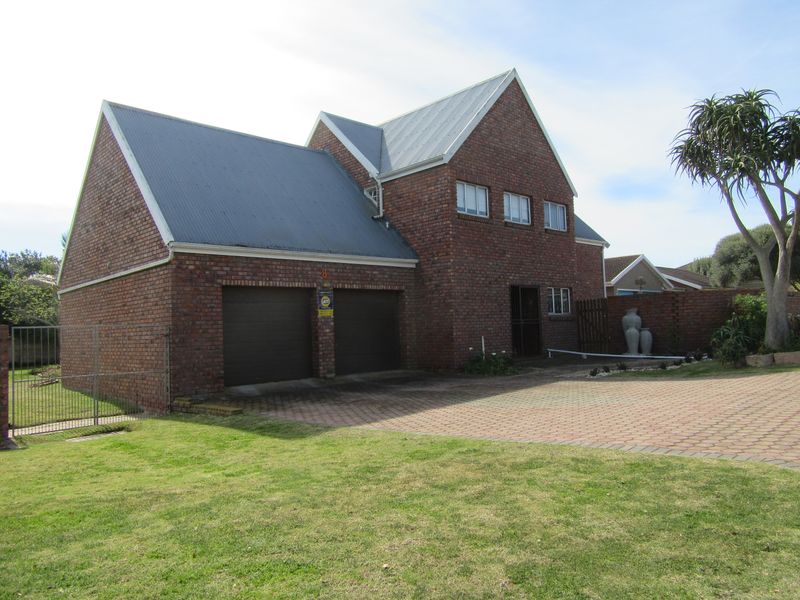A double-story brick house featuring a double garage, metal roofing, and a paved driveway set within a landscaped front garden.