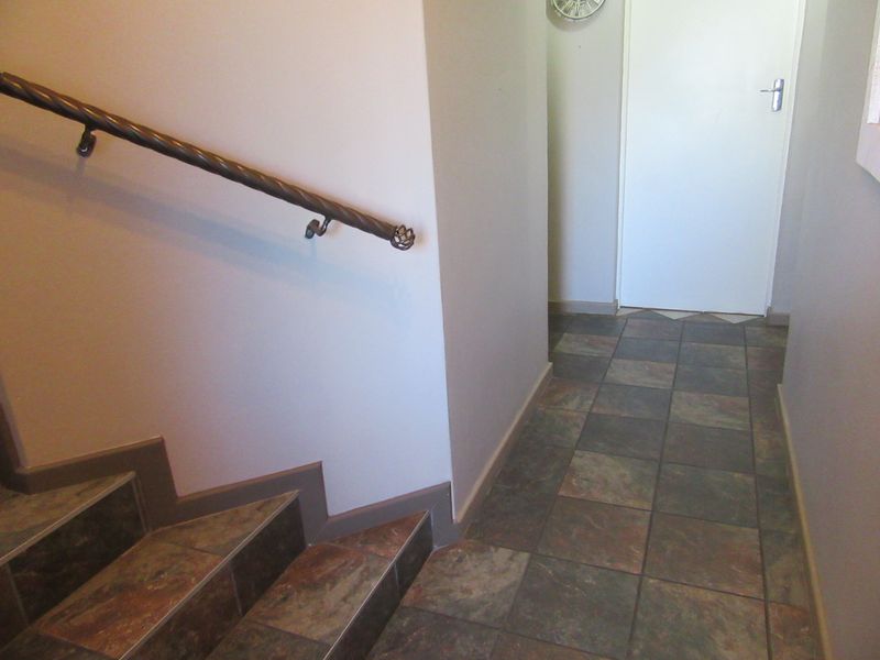 A functional hallway featuring tiled flooring and a staircase with a decorative wrought iron handrail leading to an internal door.