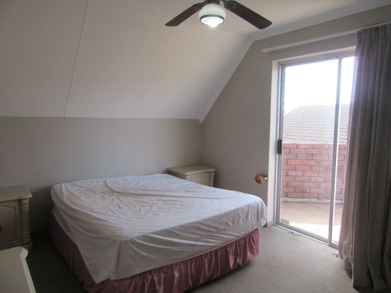 A bedroom featuring a sloped ceiling, ceiling fan, and a sliding glass door providing access to an outdoor balcony area.