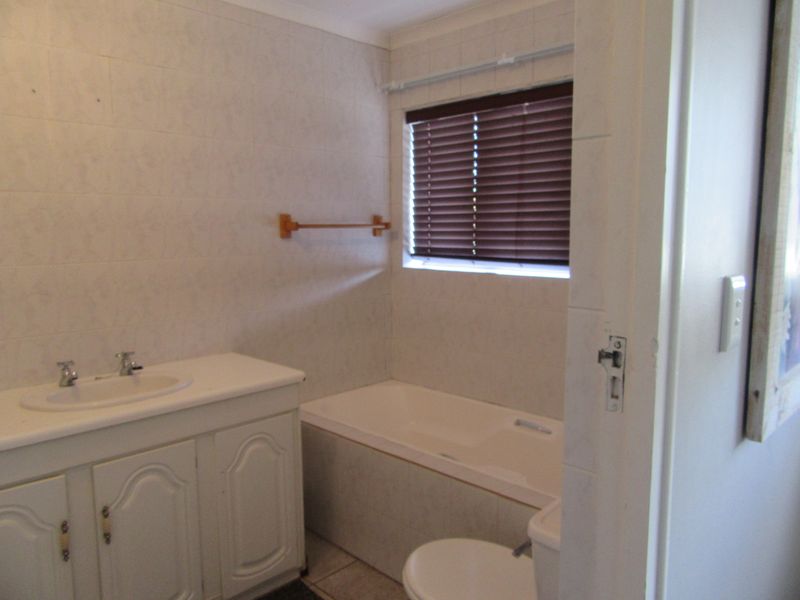 A functional bathroom featuring a built-in vanity with basin, a bathtub, and a toilet, finished with neutral wall tiling and window blinds.
