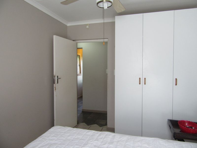 A bedroom featuring a built-in wardrobe and a ceiling fan, with a doorway leading to an adjacent hallway.