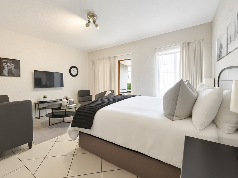 Spacious bedroom featuring tiled flooring, neutral walls, and direct access to an adjoining balcony through a glass door.
