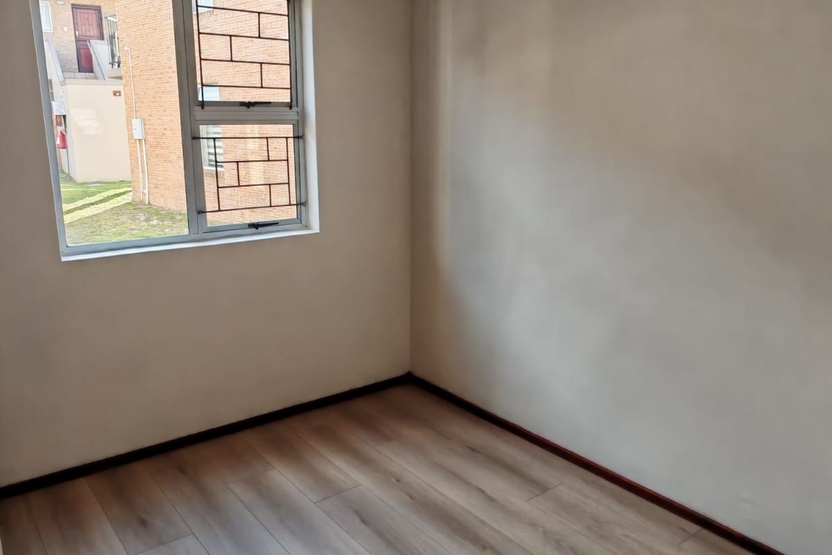 An empty bedroom featuring light-toned laminate flooring and a window fitted with security bars, offering a blank canvas for personalization.