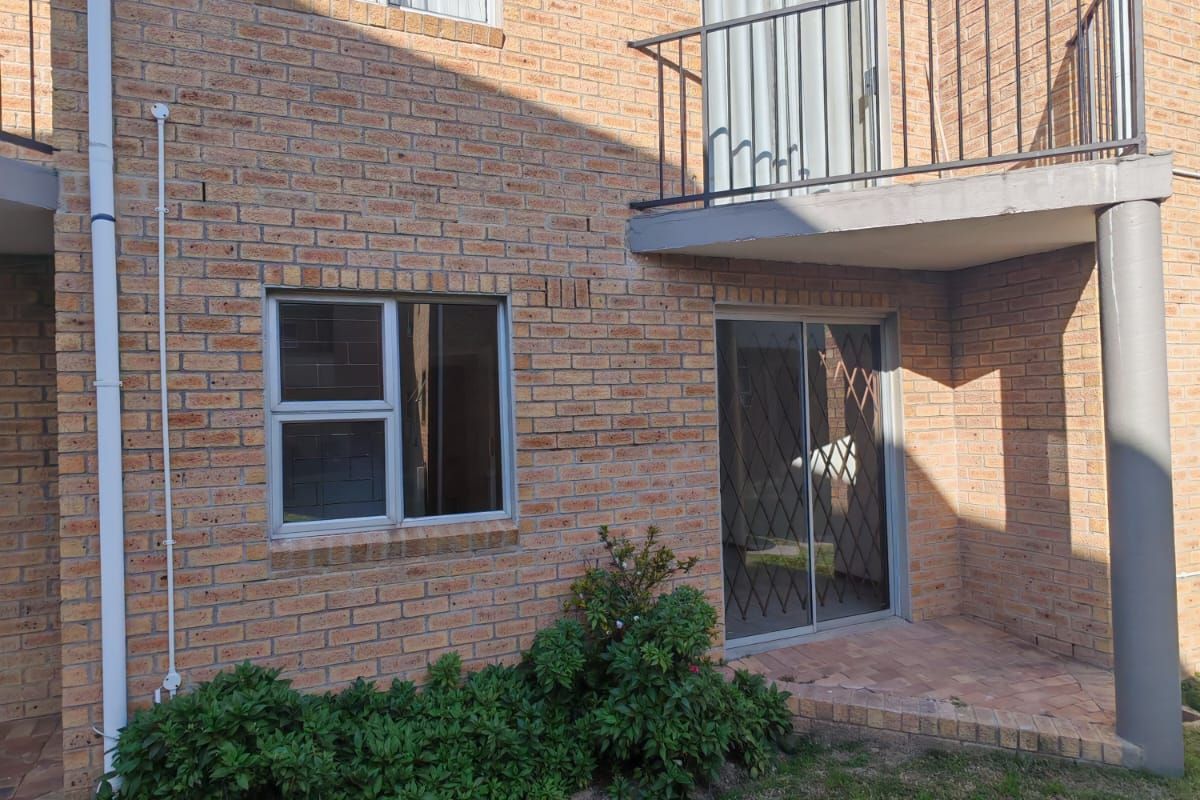 Rear view of a two-story apartment building featuring face brick construction, a private balcony with metal railing, and a ground-floor patio with security gate.