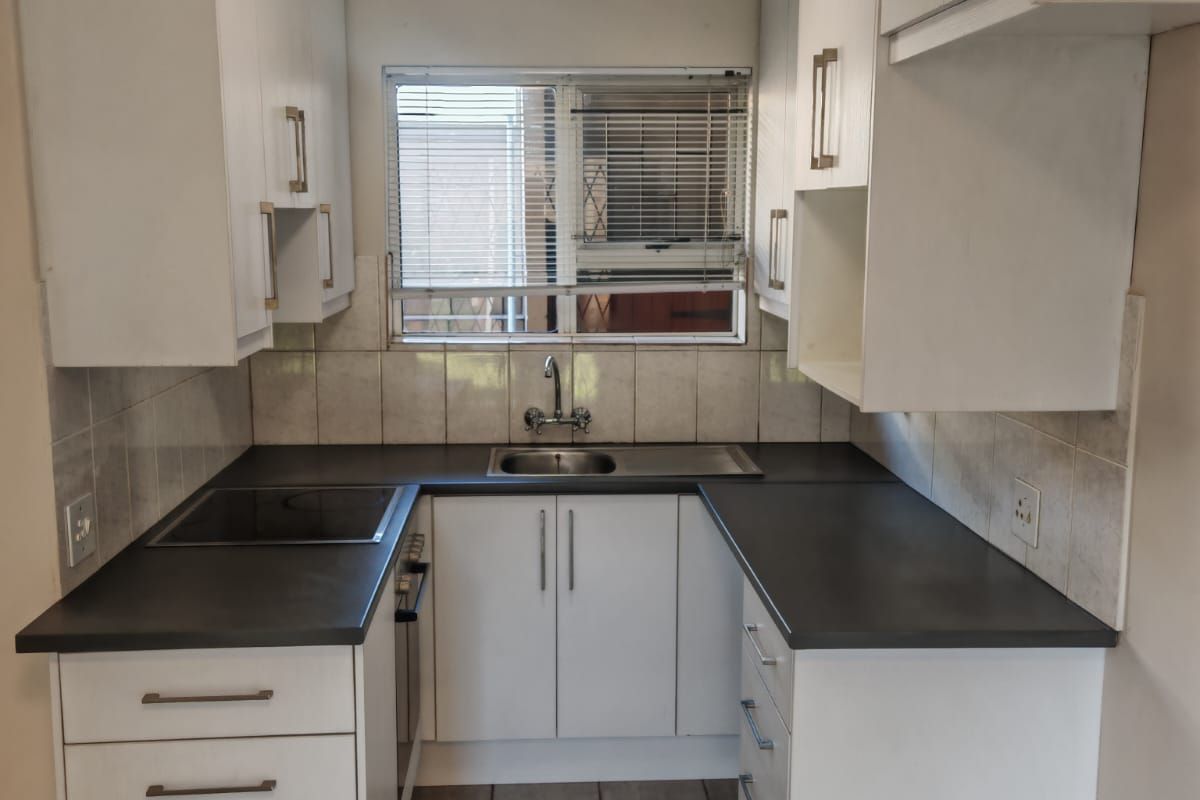 A compact, functional kitchen featuring white cabinetry, dark countertops, a built-in oven and hob, and tiled flooring.