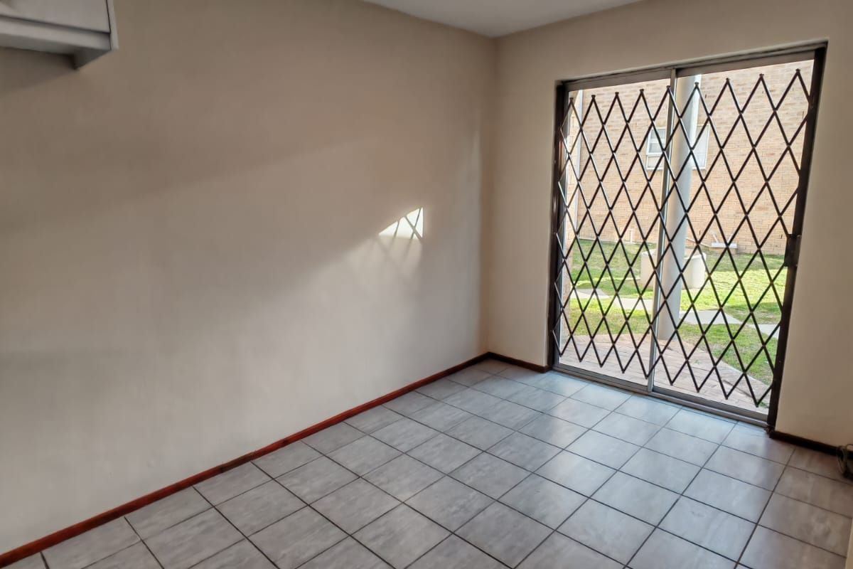 An empty living room featuring tiled flooring, a wall-mounted air conditioning unit, and a sliding glass door with a security gate leading outdoors.