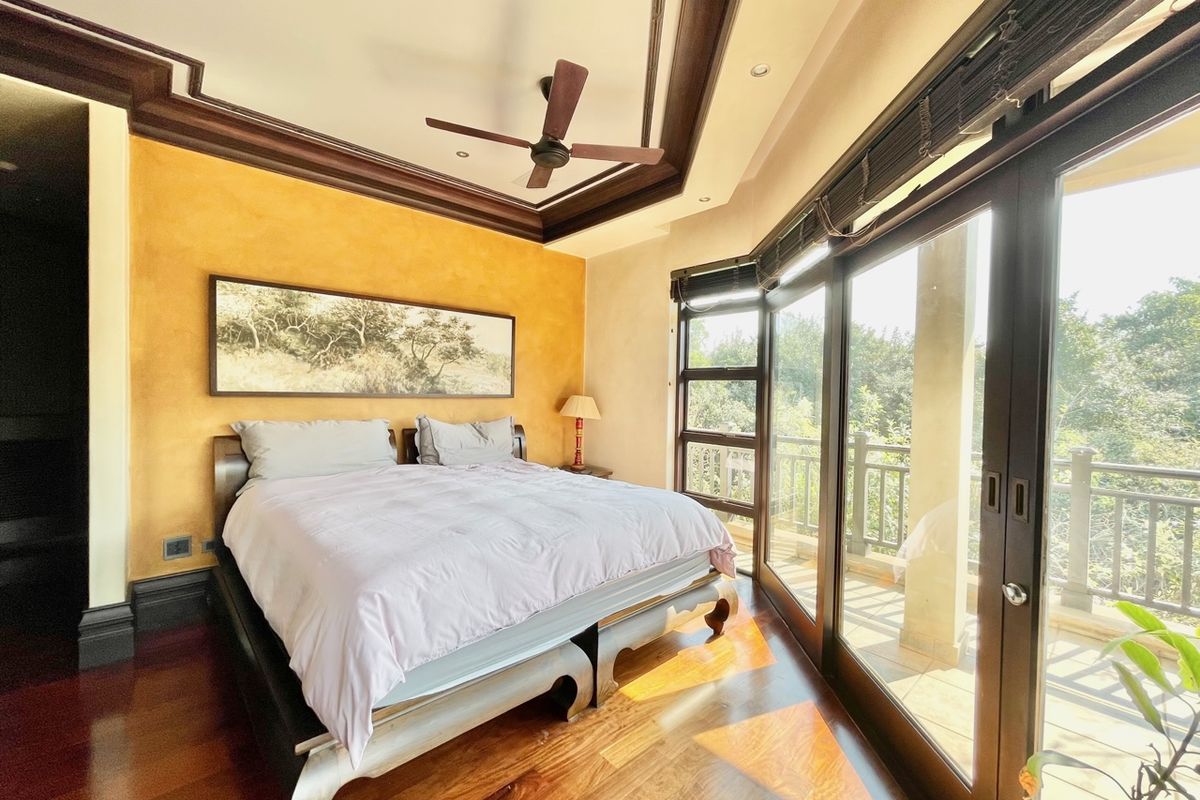 Spacious bedroom featuring a tray ceiling with a ceiling fan, rich hardwood flooring, and large glass sliding doors opening onto a private balcony.