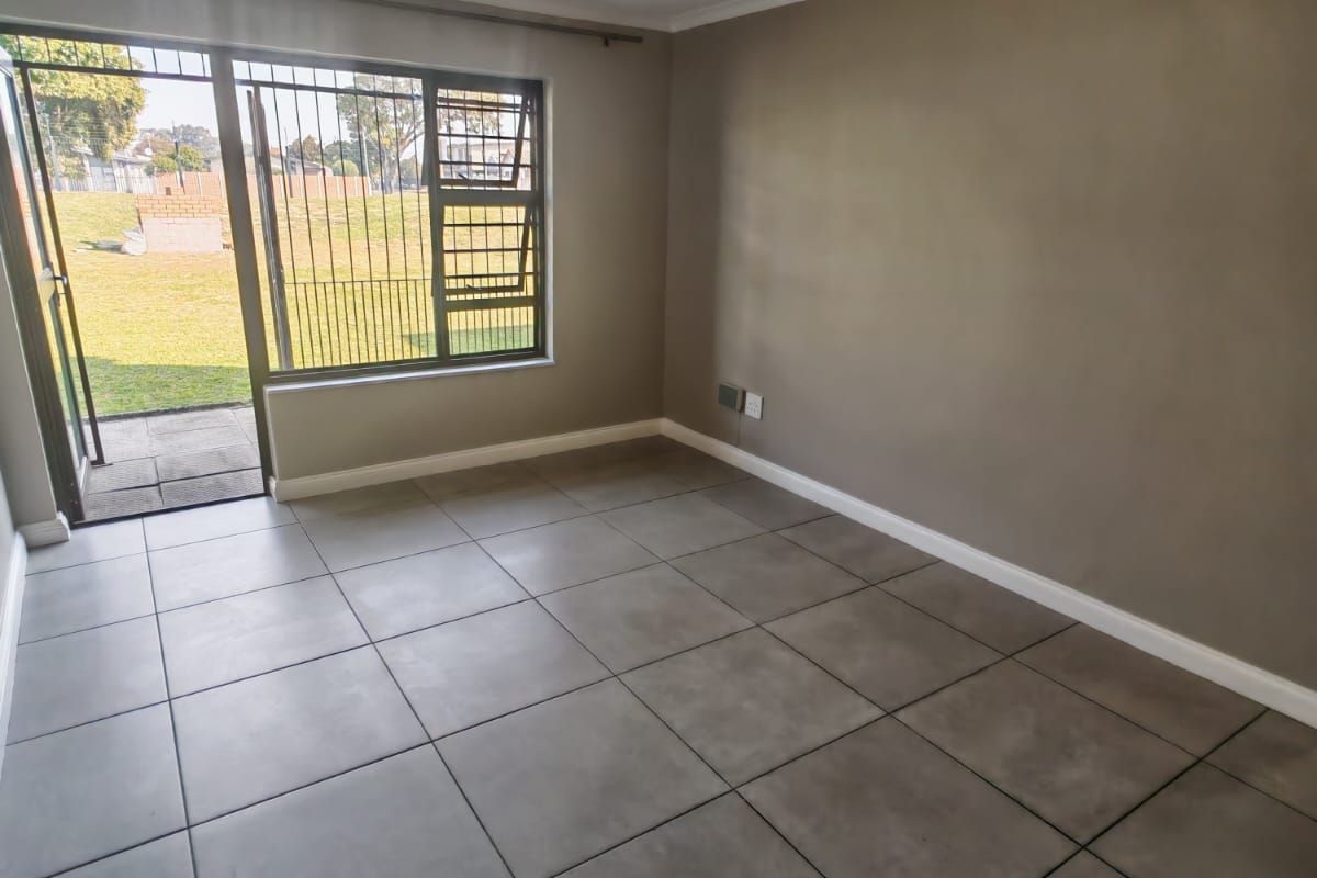A bright, empty living room featuring neutral tiled flooring, a ceiling light fixture, and a sliding glass door providing access to the outdoor area.