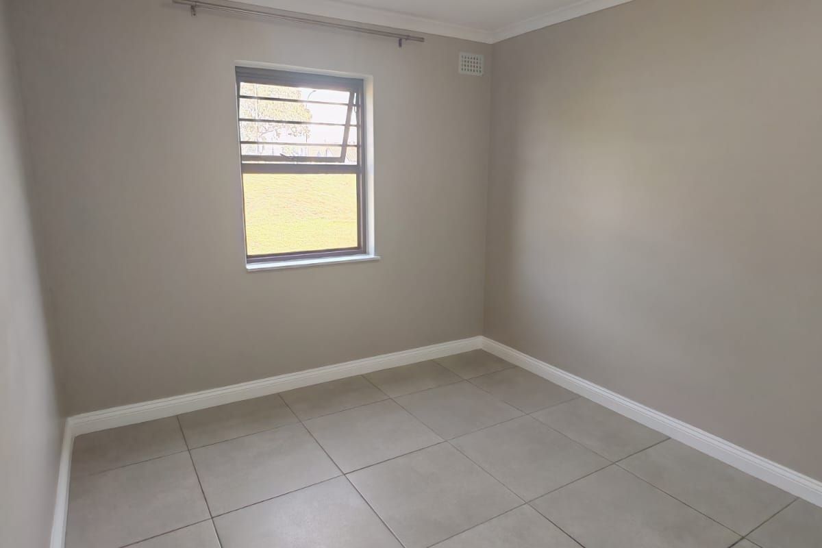 A clean, empty bedroom featuring neutral wall paint, large format floor tiles, and a louver window with a curtain rod.