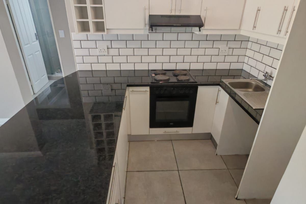 Modern kitchen featuring white cabinetry, dark granite countertops, subway tile backsplash, and integrated appliances including an oven and hob.
