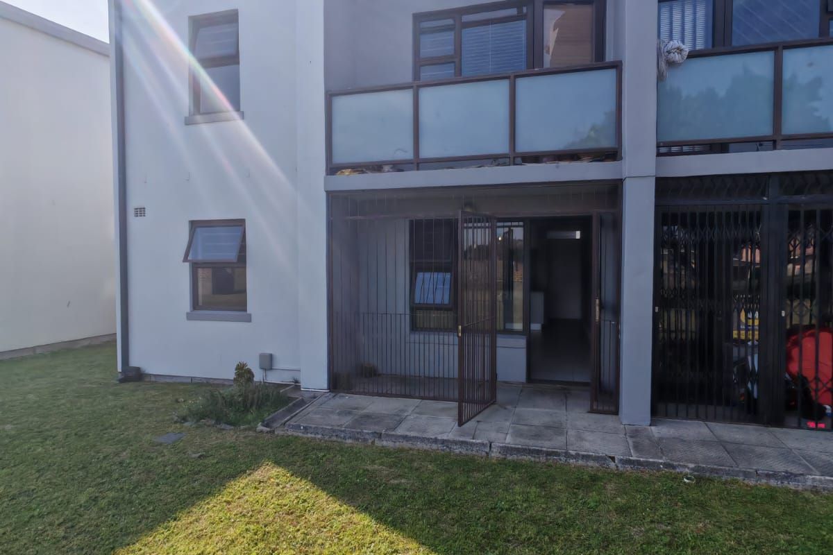 Rear view of the apartment building featuring a ground floor paved patio with security gate and an upper level balcony with glass balustrade.