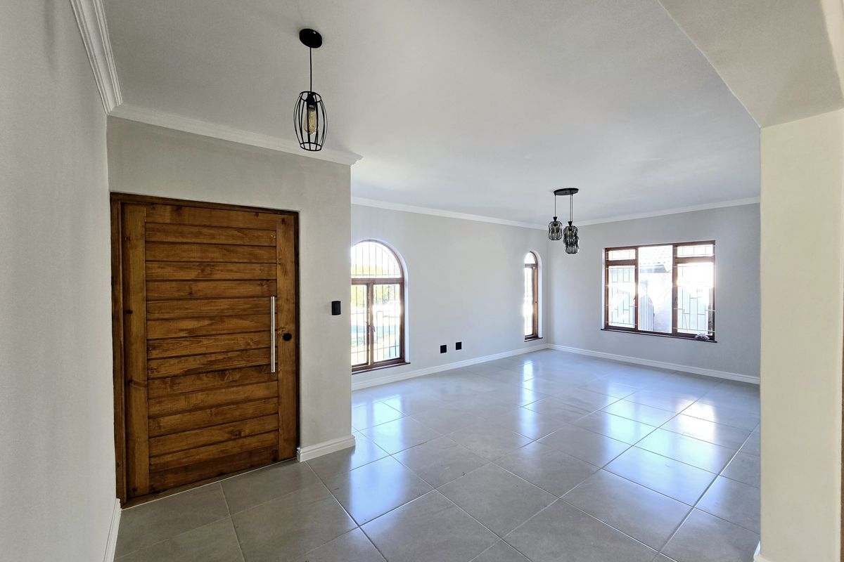 Spacious, light-filled living area featuring neutral tiled flooring, modern pendant lighting, and a solid wooden front door with arched window detailing.