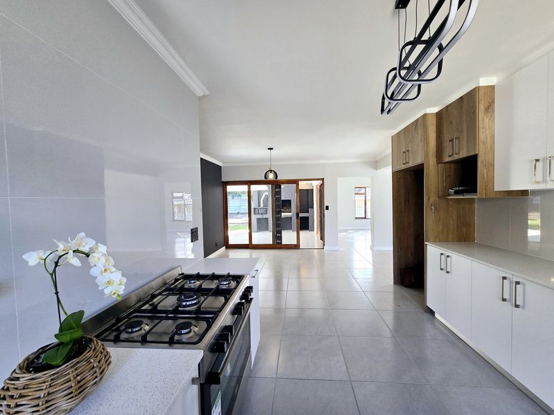 Modern open-plan kitchen featuring sleek cabinetry, stone countertops, and a gas stove, flowing seamlessly into a spacious living area with large sliding doors.