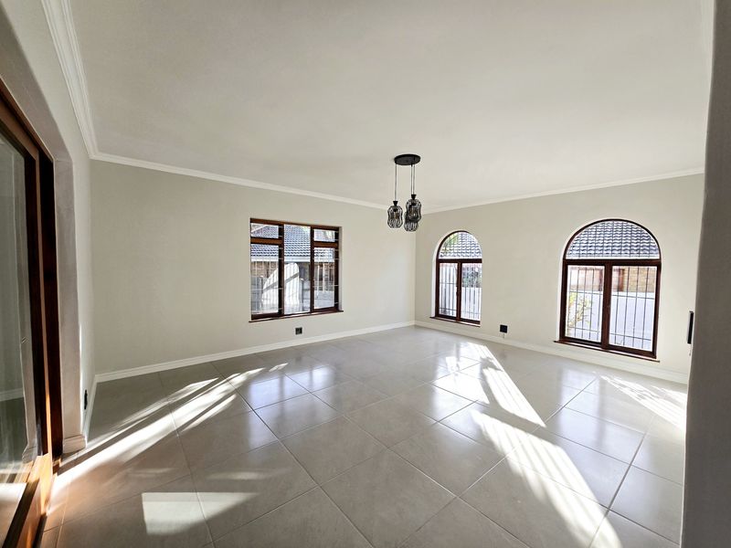 A bright, spacious, and empty living room featuring large arched windows, tiled flooring, and modern pendant lighting.
