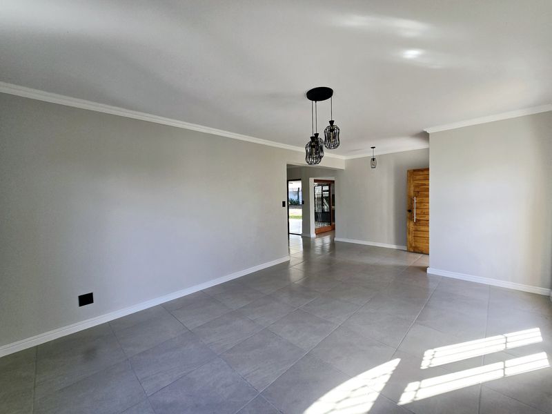 Spacious, light-filled living area featuring neutral porcelain floor tiles, modern pendant lighting, and a solid wood entrance door.