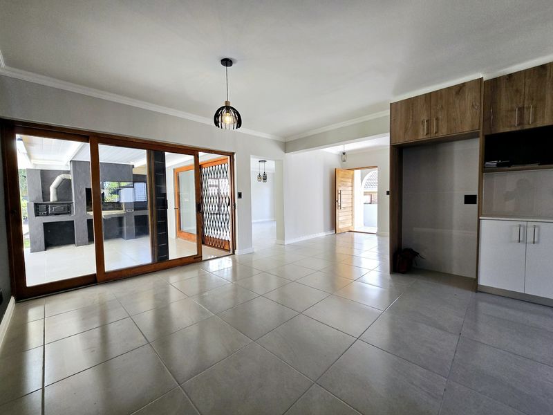 Spacious, light-filled living area featuring large sliding glass doors, neutral tiled flooring, and built-in cabinetry, offering seamless access to the outdoor patio.
