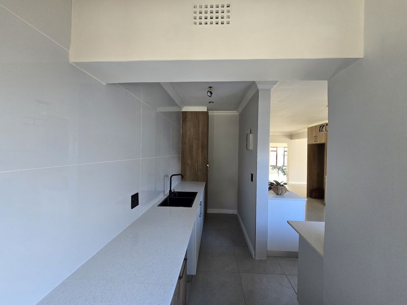 Modern kitchen featuring sleek quartz countertops, a black undermount sink, contemporary cabinetry, and neutral tiled flooring, offering a clean and functional workspace.