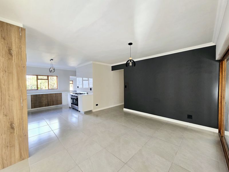 Spacious open-plan living and kitchen area featuring modern tiled floors, a contemporary kitchen with built-in appliances, and a striking dark feature wall.
