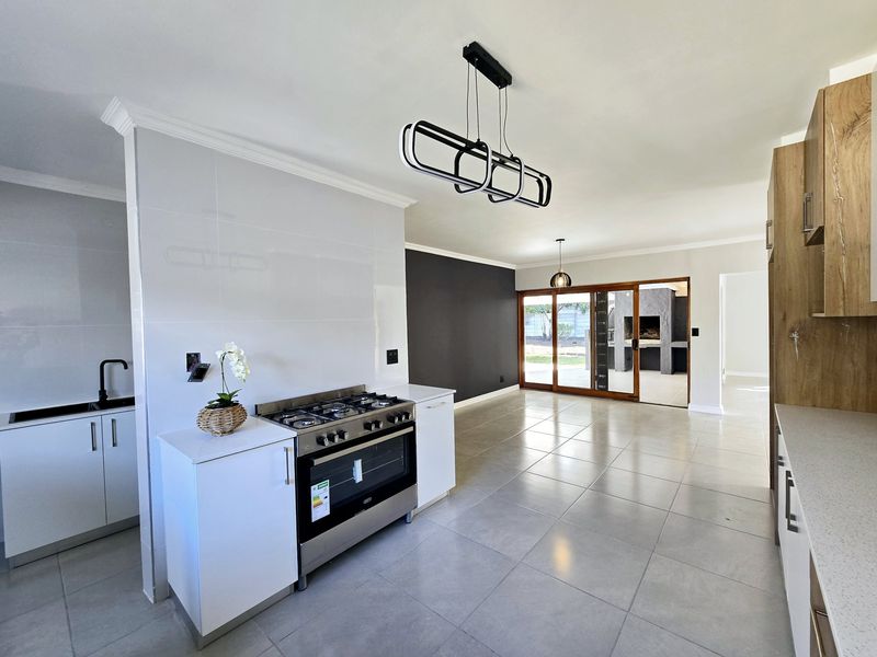 Spacious open-plan kitchen and living area featuring modern cabinetry, a gas stove, tiled floors, and seamless access to an outdoor patio with a built-in braai.