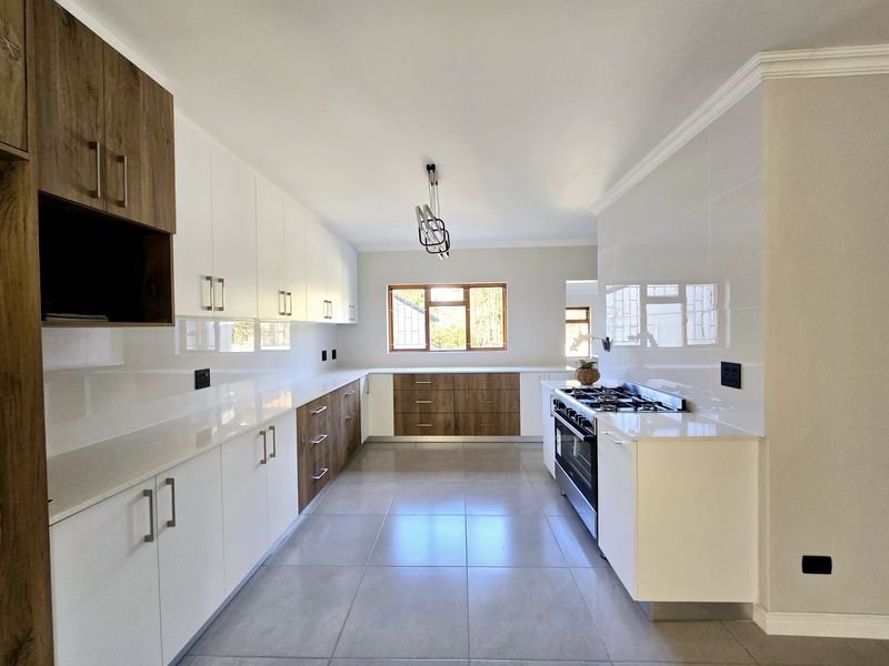 Modern, spacious kitchen featuring sleek white and wood-tone cabinetry, stone countertops, high-quality gas hob, and large format floor tiles.