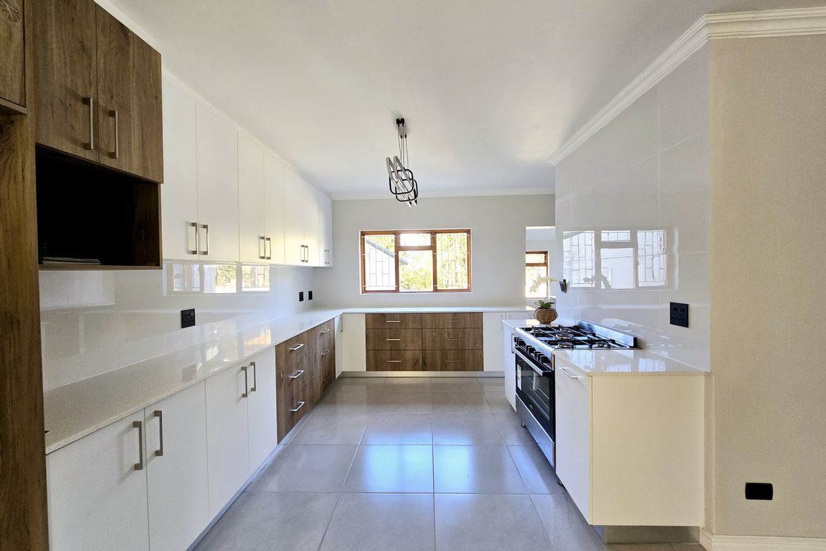 Modern, spacious kitchen featuring sleek white and wood-tone cabinetry, stone countertops, high-quality gas hob, and large format floor tiles.