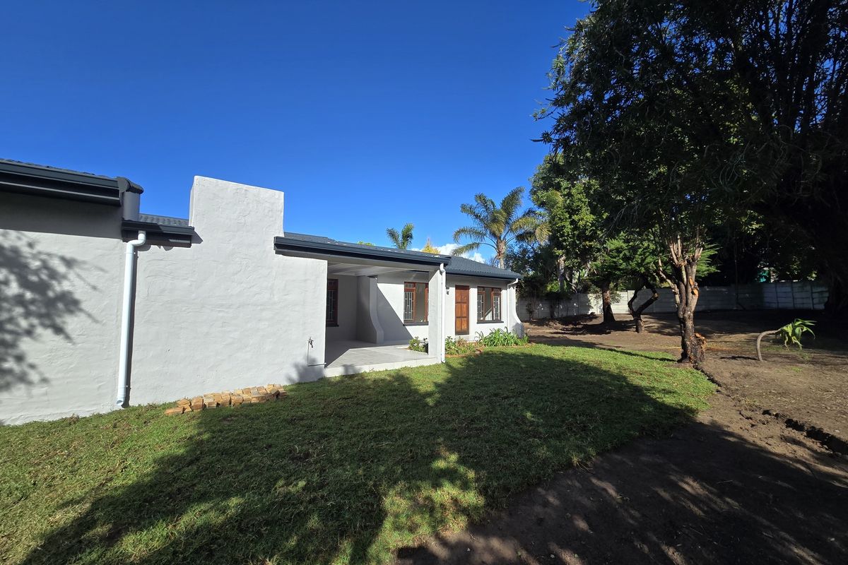 Rear view of the house featuring a covered patio area, white rendered walls, and a spacious garden with mature trees.