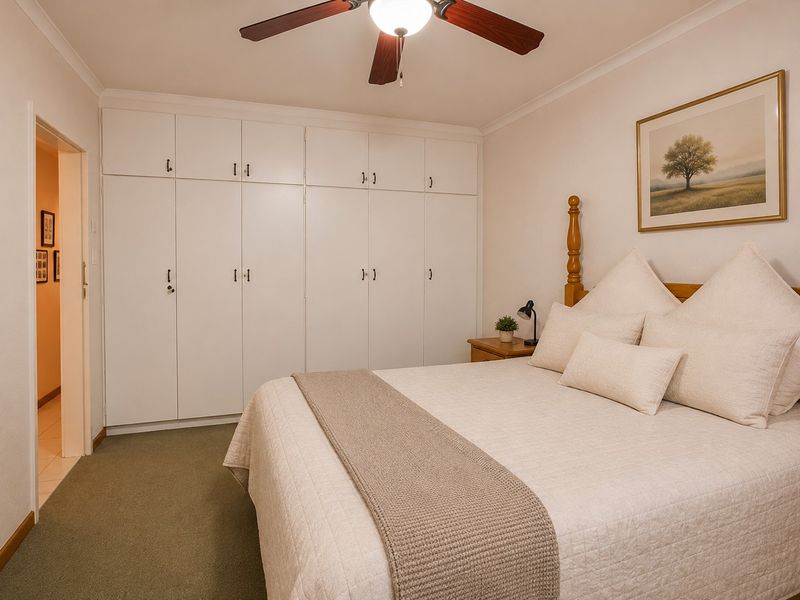 A well-maintained bedroom featuring extensive floor-to-ceiling built-in cupboards, a ceiling fan, and neutral carpeting.