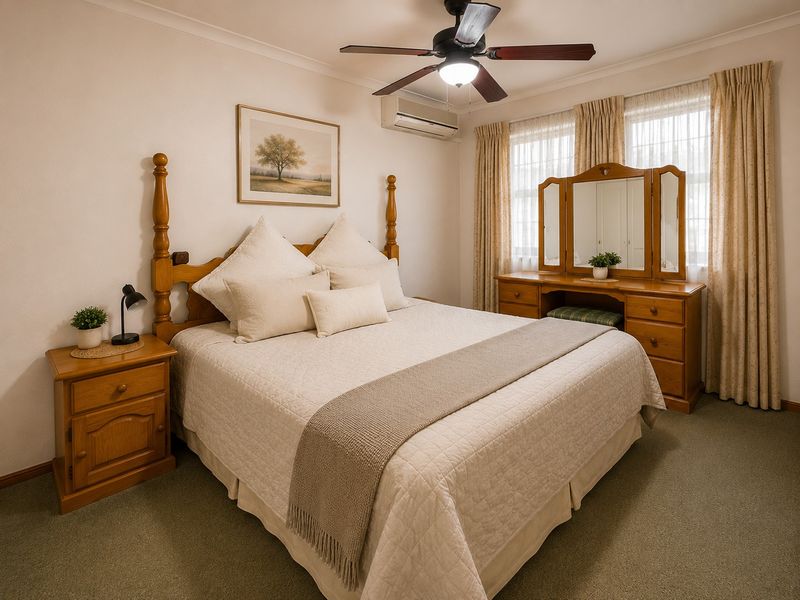 A well-maintained bedroom featuring carpet flooring, a ceiling fan, and a wall-mounted split system air conditioner for climate control.