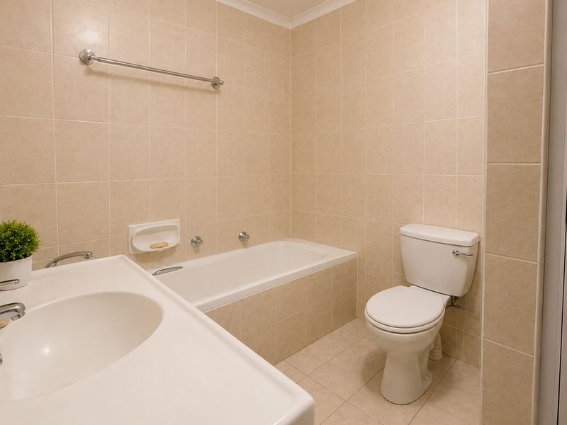 A functional bathroom featuring a built-in bathtub, vanity basin, and toilet, finished with neutral ceramic wall and floor tiles.