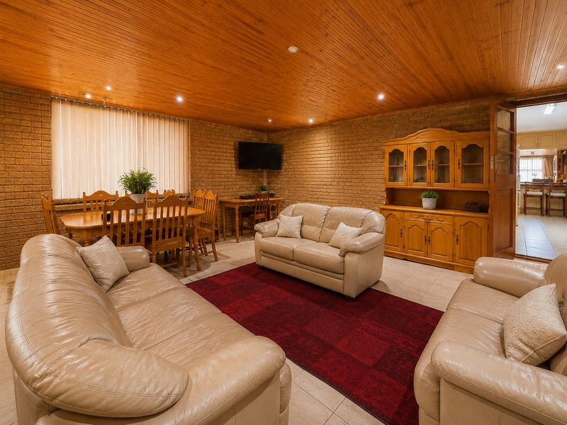Spacious open-plan living and dining area featuring exposed brick walls, a warm timber-paneled ceiling, and neutral tiled flooring.