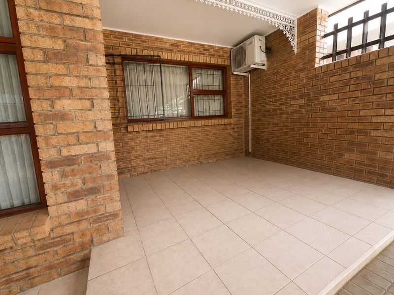 A covered patio area featuring exposed brick walls, tiled flooring, and an installed air conditioning unit, providing a functional outdoor space.