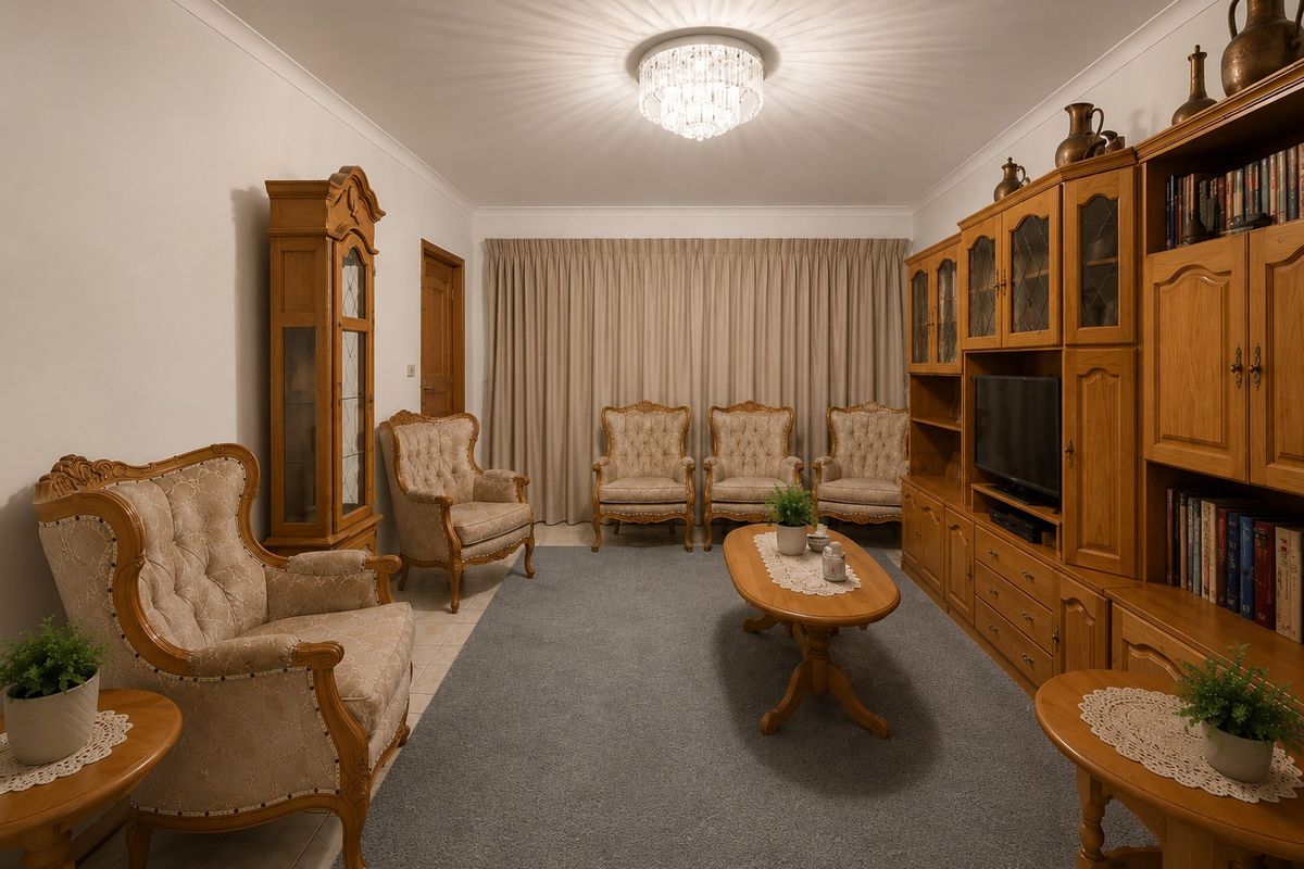 A well-maintained living room featuring tiled flooring, cove cornicing, and a central crystal chandelier, providing a classic and comfortable atmosphere.