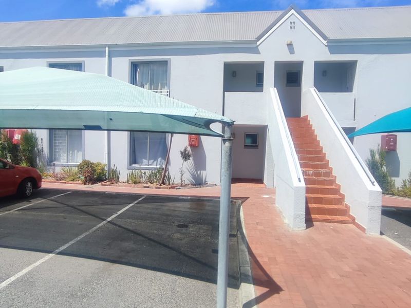 Front exterior view of the apartment building featuring a paved walkway, external staircase, and covered parking bays.