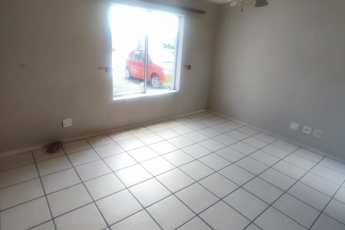 An empty living room featuring tiled flooring, a ceiling fan, and natural light from a window.
