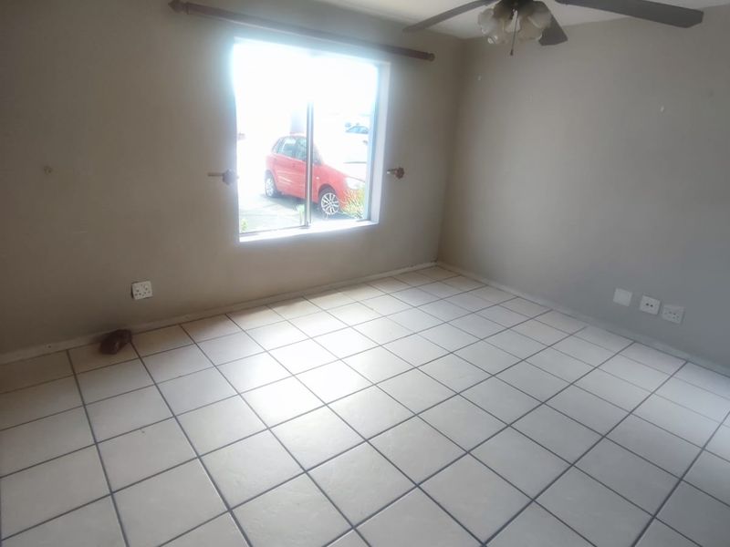 An empty living room featuring tiled flooring, a ceiling fan, and natural light from a window.