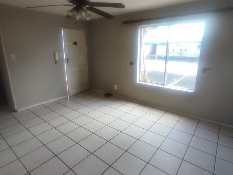 An empty living room featuring tiled flooring, a ceiling fan, and a large window providing natural light.