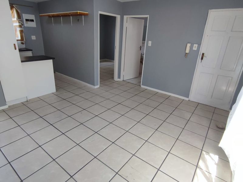 An open-plan living area featuring tiled flooring, a compact kitchen counter, and neutral grey walls, providing a blank canvas for interior design.