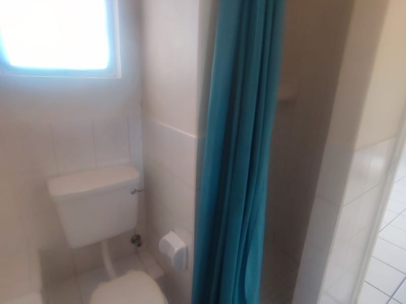 A functional bathroom featuring a toilet, shower area with curtain, and tiled finishes throughout.