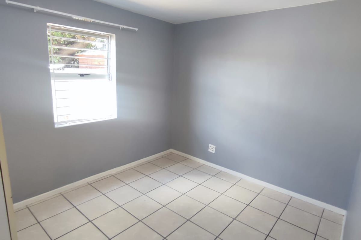A clean, empty bedroom featuring neutral grey walls, tiled flooring, and a louvered window, providing a blank canvas for personalization.