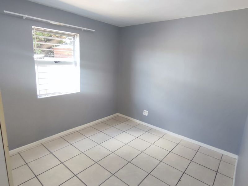 A clean, empty bedroom featuring neutral grey walls, tiled flooring, and a louvered window, providing a blank canvas for personalization.