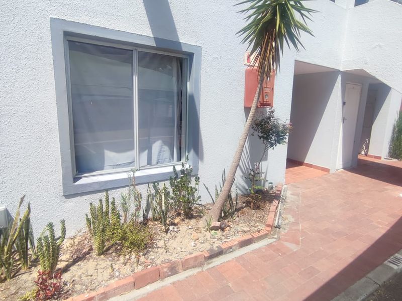 Exterior view of the apartment building featuring a paved walkway, stucco facade, and a small garden bed with a sliding window.
